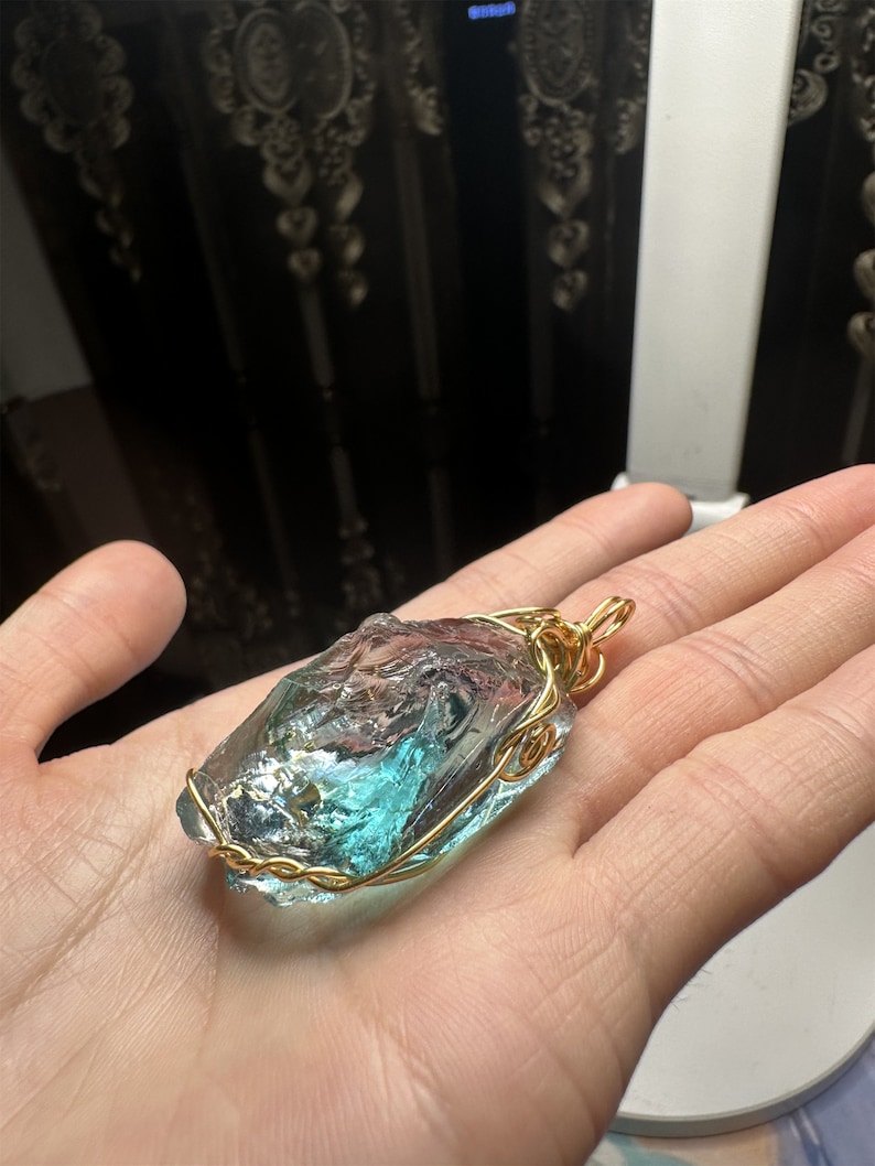 May include: A teal blue glass pendant wrapped in gold wire. The pendant is irregularly shaped and has a rough, natural texture.
