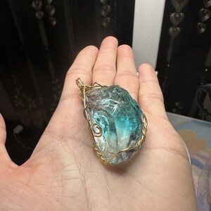May include: A teal and green crystal pendant wrapped in gold wire. The crystal is irregularly shaped and has a rough texture.