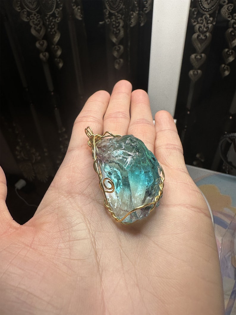 May include: A teal and green crystal pendant wrapped in gold wire. The crystal is irregularly shaped and has a rough texture.