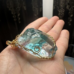 May include: A large, clear, blue and green crystal pendant wrapped in gold wire. The pendant is hanging from a gold chain.