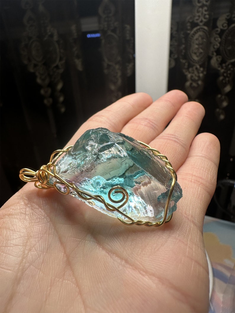 May include: A large, clear, blue and green crystal pendant wrapped in gold wire. The pendant is hanging from a gold chain.