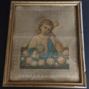 Puede incluir: Una impresión religiosa enmarcada que presenta a un niño pequeño sosteniendo un globo terráqueo y una cruz, rodeado de rosas. La impresión está en un marco dorado con un passe-partout blanco y un borde de encaje.