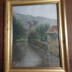 Może przedstawiać: Ramowany obraz pastelowy przedstawiający mglisty krajobraz z rzeką, kamiennym mostem i wsią w tle. Obraz jest podpisany i datowany "9-1947".