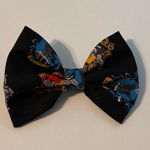 May include: Black bow tie with a colorful print of the Hogwarts house crests. The crests are for Gryffindor, Hufflepuff, Slytherin, and Ravenclaw.