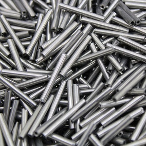 May include: A close-up image of a pile of silver metal rods. The rods are all the same size and shape, and they are arranged in a random pattern.