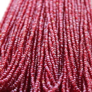 May include: Close-up of a bundle of small, faceted beads in a deep red colour. The beads are strung together, creating a dense, textured appearance. The beads are likely for jewellery making.
