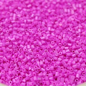 Puede incluir: Primer plano de un montón de pequeñas cuentas de semillas de color rosa brillante. Las cuentas son cilíndricas con un agujero en el centro y están densamente empaquetadas. Las cuentas tienen un acabado ligeramente brillante.