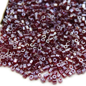 Puede incluir: Un montón grande de pequeñas cuentas de vidrio de color rojo oscuro. Las cuentas son hexagonales y tienen un brillo metálico.