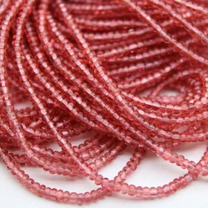 May include: A close-up of a strand of small, round, translucent pink glass beads. The beads are arranged in a loose pile, showing their individual shape and texture.