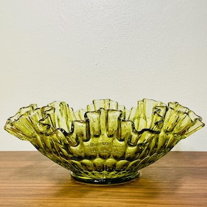 May include: A green glass bowl with a ruffled edge and a textured bottom. The bowl is made of clear glass with a green tint.