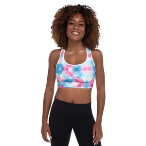 Könnte beinhalten: Sport-BH mit geometrischem Muster in Rosa, Blau und Weiß. Der BH hat einen weißen Besatz und ein Racerback-Design. Das Model trägt schwarze Leggings.