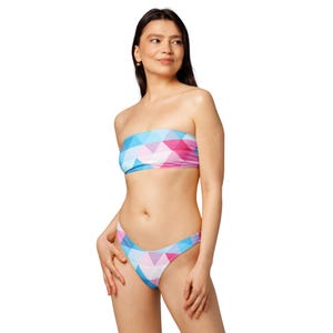 Puede incluir: Conjunto de bikini de dos piezas con un diseño geométrico en tonos azules, rosas y blancos. El top sin tirantes y la braguita de talle bajo crean un look de baño moderno. El bikini está hecho de una tela suave y elástica.