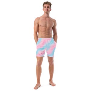 Könnte beinhalten: Badeshorts mit einem Batikmuster in Rosa und Hellblau. Die Shorts haben einen Kordelzug in der Taille und Taschen. Das Model steht mit den Händen in den Taschen.