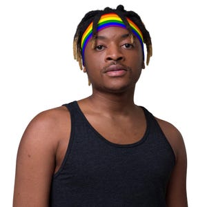 Könnte beinhalten: Ein schwarzes Tanktop. Ein regenbogenfarbenes Stirnband wird auf dem Kopf getragen. Das Stirnband hat die Farben des Regenbogens: rot, orange, gelb, grün, blau und lila. Die Person hat dunkle Haare und Haut.