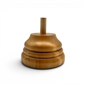 May include: A light brown wooden display stand featuring a wide, tiered circular base with a smooth, polished finish and a single, centered vertical cylindrical post extending upward from the top, designed for holding items securely in place.