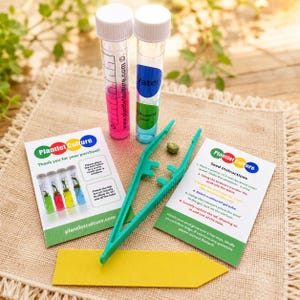 May include: A plant propagation kit featuring two clear plastic test tubes with white lids, one containing pink liquid and one with blue liquid labelled Water and Antibacterial Soap. Includes green plastic tweezers, a yellow plant marker, and two cards.