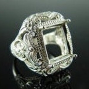 May include: Silver ring with an ornate design and a square empty setting for a gemstone.