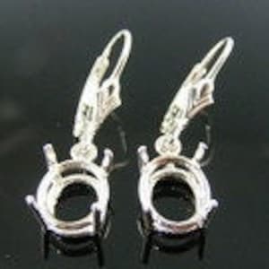 May include: A pair of silver earring settings with a teardrop-shaped oval bezel. The settings are designed to hold a gemstone or other embellishment.