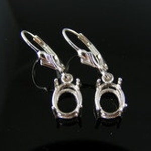 May include: A pair of silver earring settings with oval-shaped bezels. The settings are designed to hold gemstones or other embellishments.