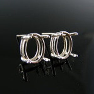 May include: A pair of silver oval earring settings. The settings are designed to hold a gemstone or other embellishment.