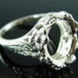 May include: Silver ring setting with an ornate design and a large oval-shaped opening for a stone. The setting has a delicate floral pattern.