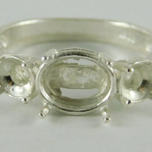 May include: Silver ring with three oval-shaped settings for gemstones. The ring is designed to hold three stones, with the center stone being larger than the two side stones.