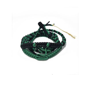 May include: A black and green braided rope with a tassel. The rope is coiled into a circle and has two green eyes on the top.