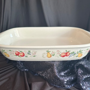 May include: White ceramic baking dish with a floral design featuring pears, apples, and berries. The dish has a slightly rounded rectangular shape with a rim.