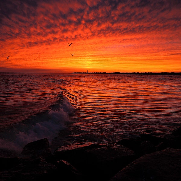 A rolling wave crashes on jetty rocks as an amazing sunset sky lights up the summer coastline in Cape May, New Jersey.