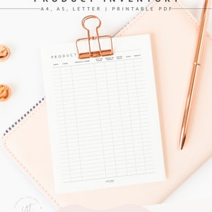 May include: A printable product inventory sheet with columns for date, code, product name, on hand, made to order, sales price, cost, and profit. The sheet is attached to a pink notebook with a gold binder clip.
