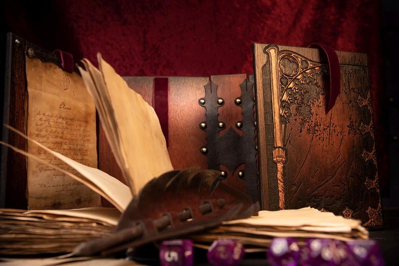 May include: A collection of handcrafted, antique-style journals and books with aged paper pages. The journals feature intricate wooden covers with metal studs and decorative carvings. A leather quill and purple dice are in the foreground.