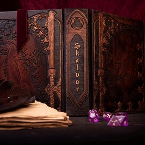 May include: A wooden Skalvor game master screen with intricate carvings and a dark brown finish. A stack of aged paper, a leather accessory, and purple dice are in the foreground. A burgundy ribbon is attached.