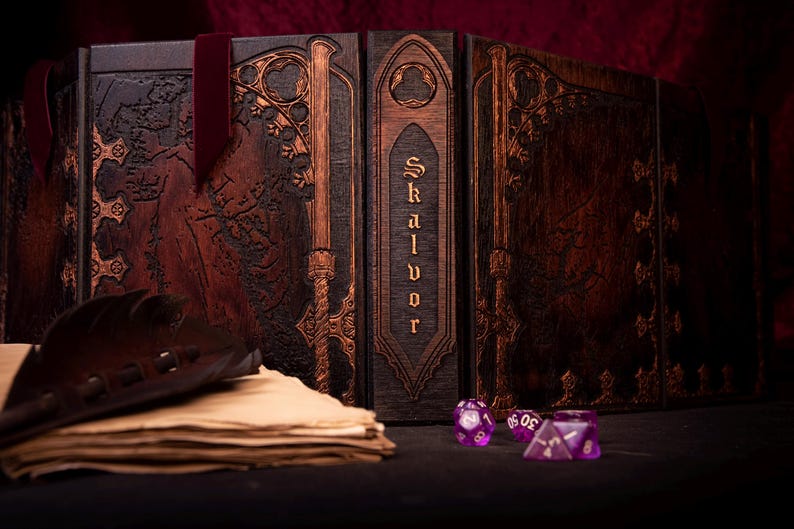 May include: A wooden Skalvor game master screen with intricate carvings and a dark brown finish. A stack of aged paper, a leather accessory, and purple dice are in the foreground. A burgundy ribbon is attached.