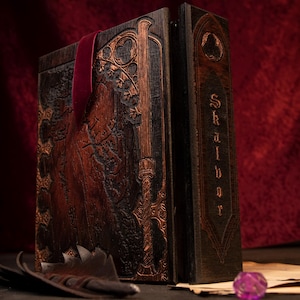 May include: A large, ornate wooden book with intricate carvings and a burgundy ribbon bookmark. The book's cover features detailed relief work and a metallic gold accent. The spine reads "Skalbor" in a gothic font. A feather and dice are in the foreground.
