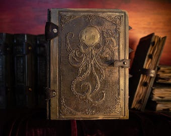 Op de afbeelding: Een donkerbruin lederen gebonden dagboek met een gegraveerd ontwerp van een octopus met een schedelkop. Het dagboek heeft metalen accenten en een sluiting met een band.