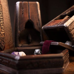 Könnte beinhalten: Eine Holzkiste mit Samtfütterung und einem Etikett mit der Aufschrift "Alchemy Featherstone". Die Kiste ist geöffnet und enthält mehrere Würfel.