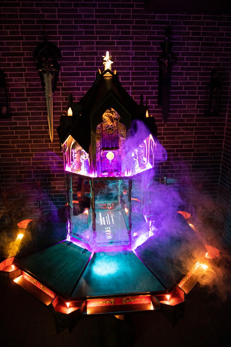 May include: A dark wooden gothic-style structure with a purple and blue light emanating from the base. The structure is surrounded by smoke and has a small book with the text "W4A5" on the top level.