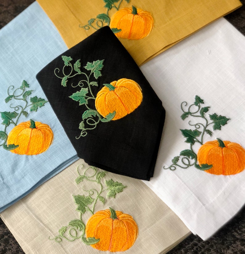 May include: Set of four embroidered linen napkins featuring a pumpkin vine design. The napkins are in various colours, including blue, white, black, and beige.