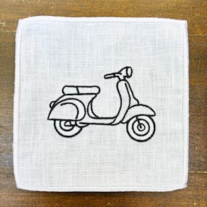 May include: A white square cloth with a black embroidered outline of a vintage scooter. The scooter design includes the handlebars, seat, and wheels. The cloth has a textured appearance and a white border.
