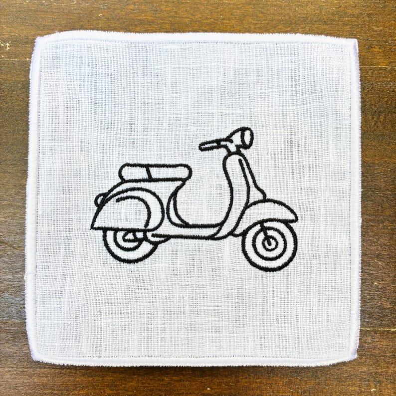 May include: A white square cloth with a black embroidered outline of a vintage scooter. The scooter design includes the handlebars, seat, and wheels. The cloth has a textured appearance and a white border.