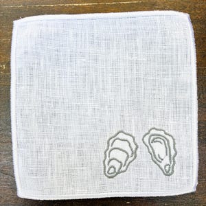 May include: White linen handkerchief with a gray embroidered oyster design. The square handkerchief has a stitched border and a textured appearance. The oyster design is on the lower right corner.