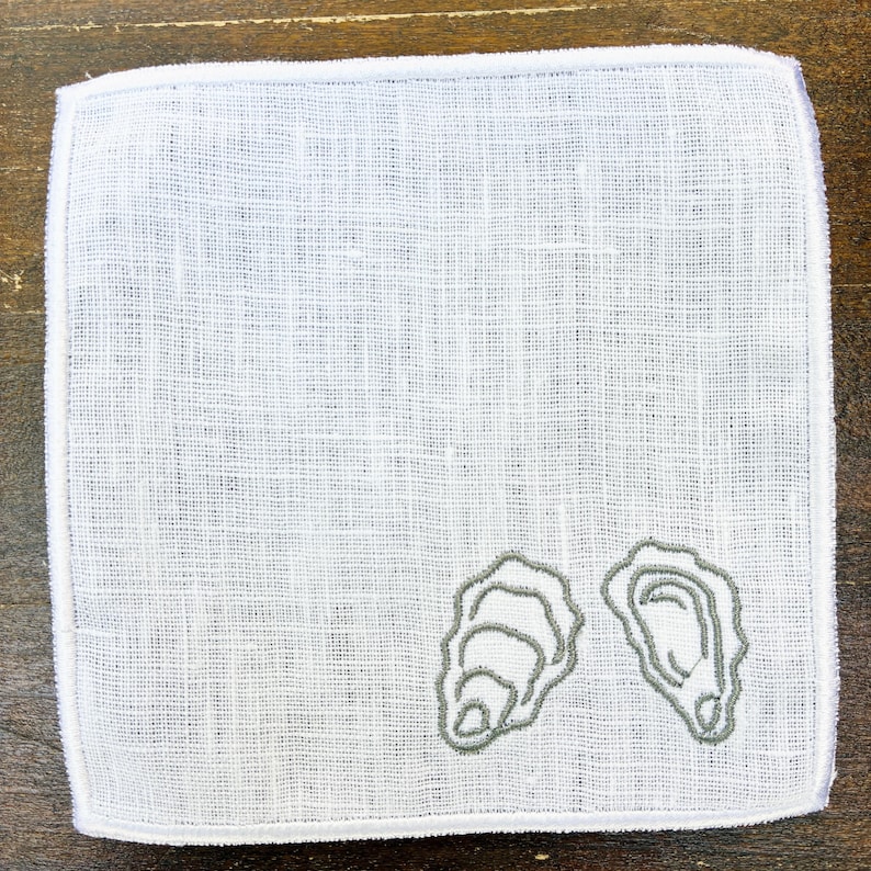 May include: White linen handkerchief with a gray embroidered oyster design. The square handkerchief has a stitched border and a textured appearance. The oyster design is on the lower right corner.