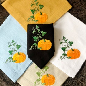 May include: Set of four kitchen towels featuring embroidered pumpkins and vines. The towels are in a variety of colours, including yellow, blue, white and black.