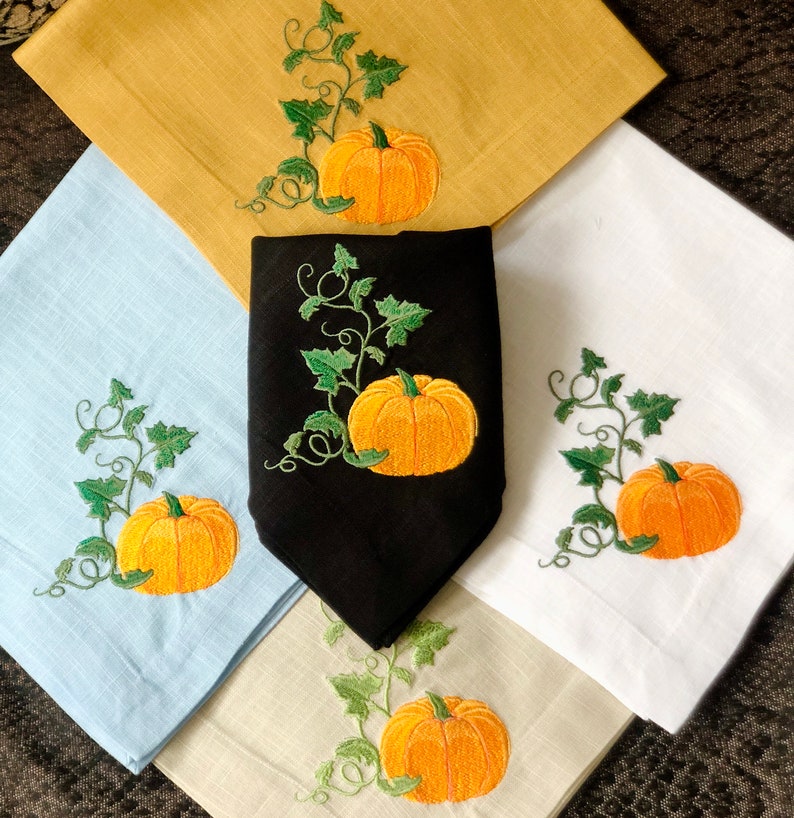 May include: Set of four kitchen towels featuring embroidered pumpkins and vines. The towels are in a variety of colours, including yellow, blue, white and black.
