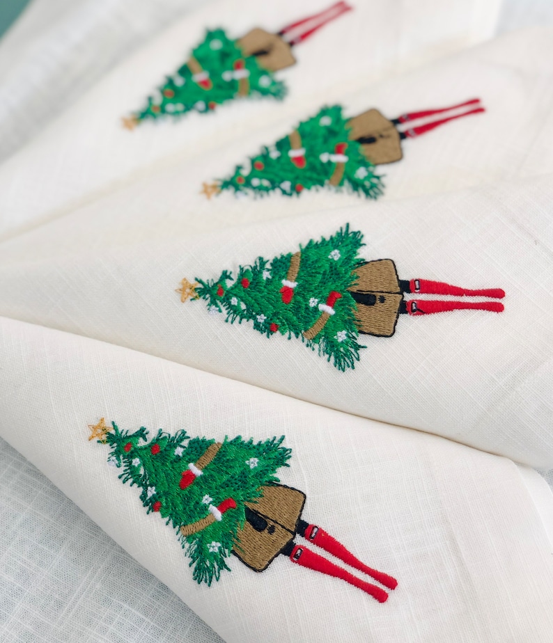 May include: Set of four white linen napkins featuring embroidered Christmas trees and figures with red legs. Each napkin has a green Christmas tree with brown decorations and a gold star on top.