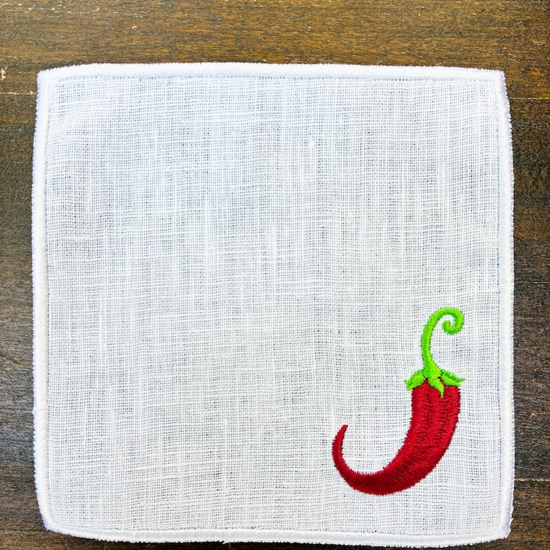 May include: White linen handkerchief with a red chili pepper embroidered in the corner. The chili pepper has a green stem and a curved shape. The handkerchief has a white border and a textured weave.