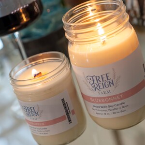Pu&ograve; includere: Due barattoli di vetro con candele accese all'interno. I barattoli hanno etichette che recitano "Free Reign Farm" e "Bluebonnet" con il testo "Wood Wick Soy Candle".