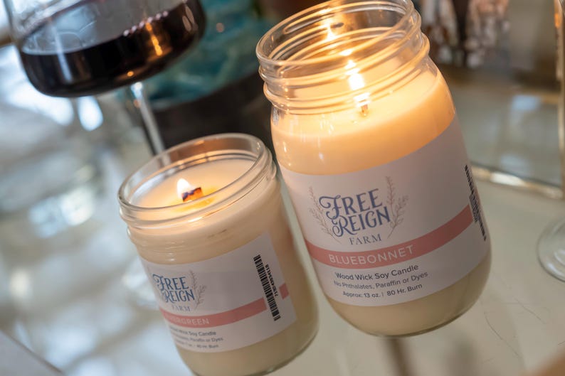 Pu&ograve; includere: Due barattoli di vetro con candele accese all'interno. I barattoli hanno etichette che recitano "Free Reign Farm" e "Bluebonnet" con il testo "Wood Wick Soy Candle".
