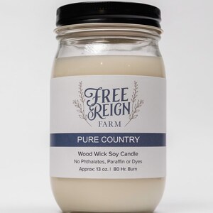 Pu&ograve; includere: Una candela di vetro in un barattolo con un coperchio nero. L'etichetta recita "FREE REIGN FARM PURE COUNTRY Wood Wick Soy Candle No Phthalates, Paraffin or Dyes Approx: 13 oz. | 80 Hr. Burn"