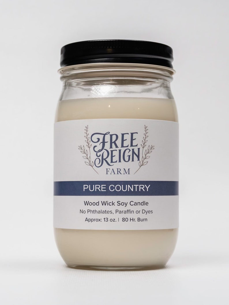Pu&ograve; includere: Una candela di vetro in un barattolo con un coperchio nero. L'etichetta recita "FREE REIGN FARM PURE COUNTRY Wood Wick Soy Candle No Phthalates, Paraffin or Dyes Approx: 13 oz. | 80 Hr. Burn"